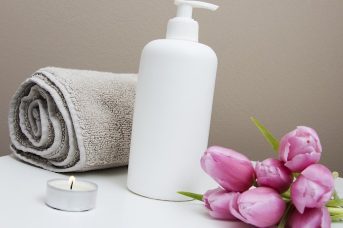 Wellness still life with a white pump bottle, rolled towel, lit candle, and pink tulips